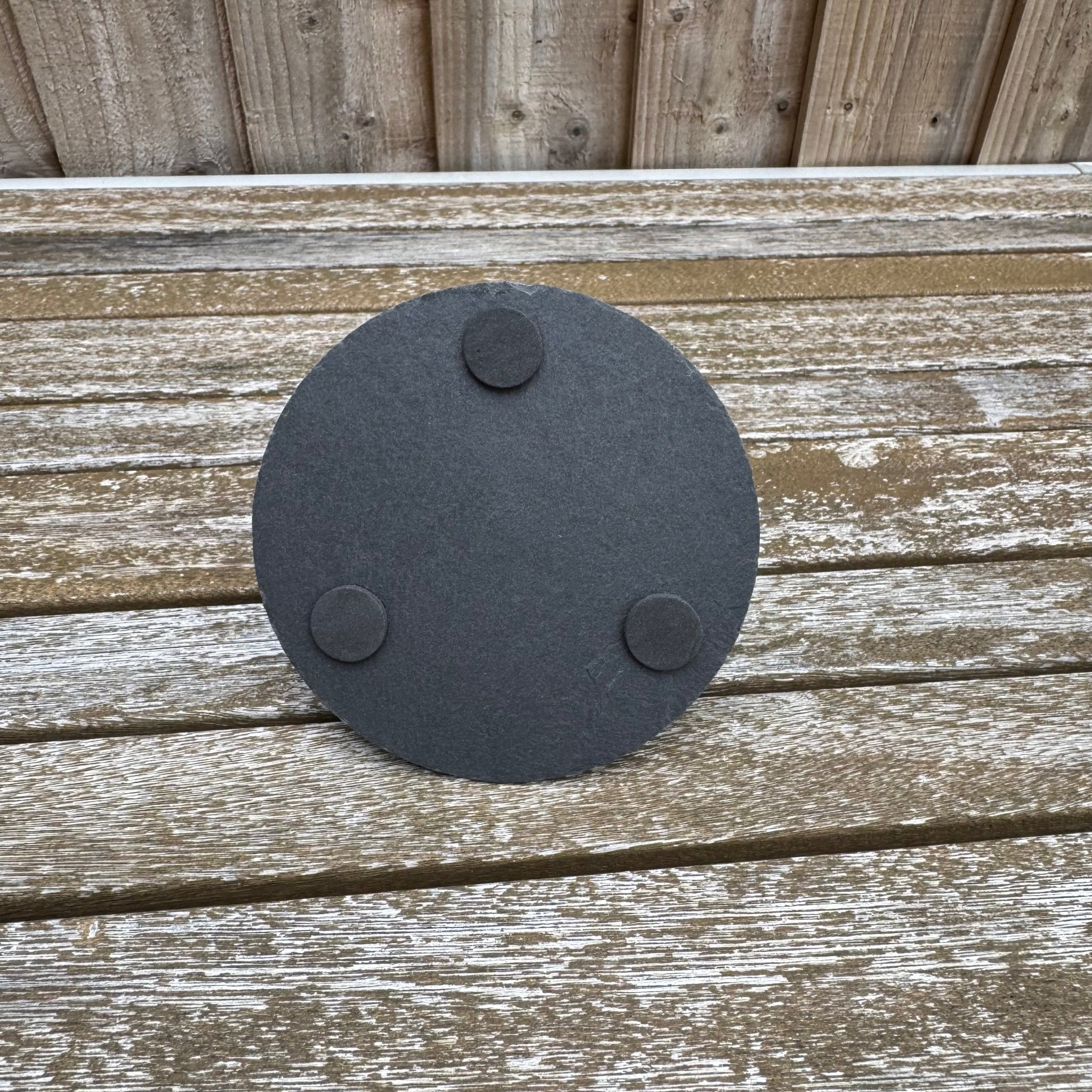 Reverse side of round slate coaster showing three rubber feet, on a wooden surface – slate coaster – Etch 'N' Shine