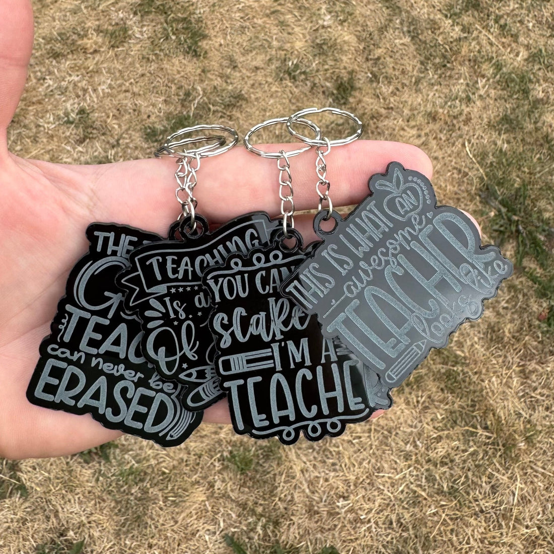 Three black acrylic keyrings with engraved text held in a hand – teacher keyrings – Etch 'N' Shine