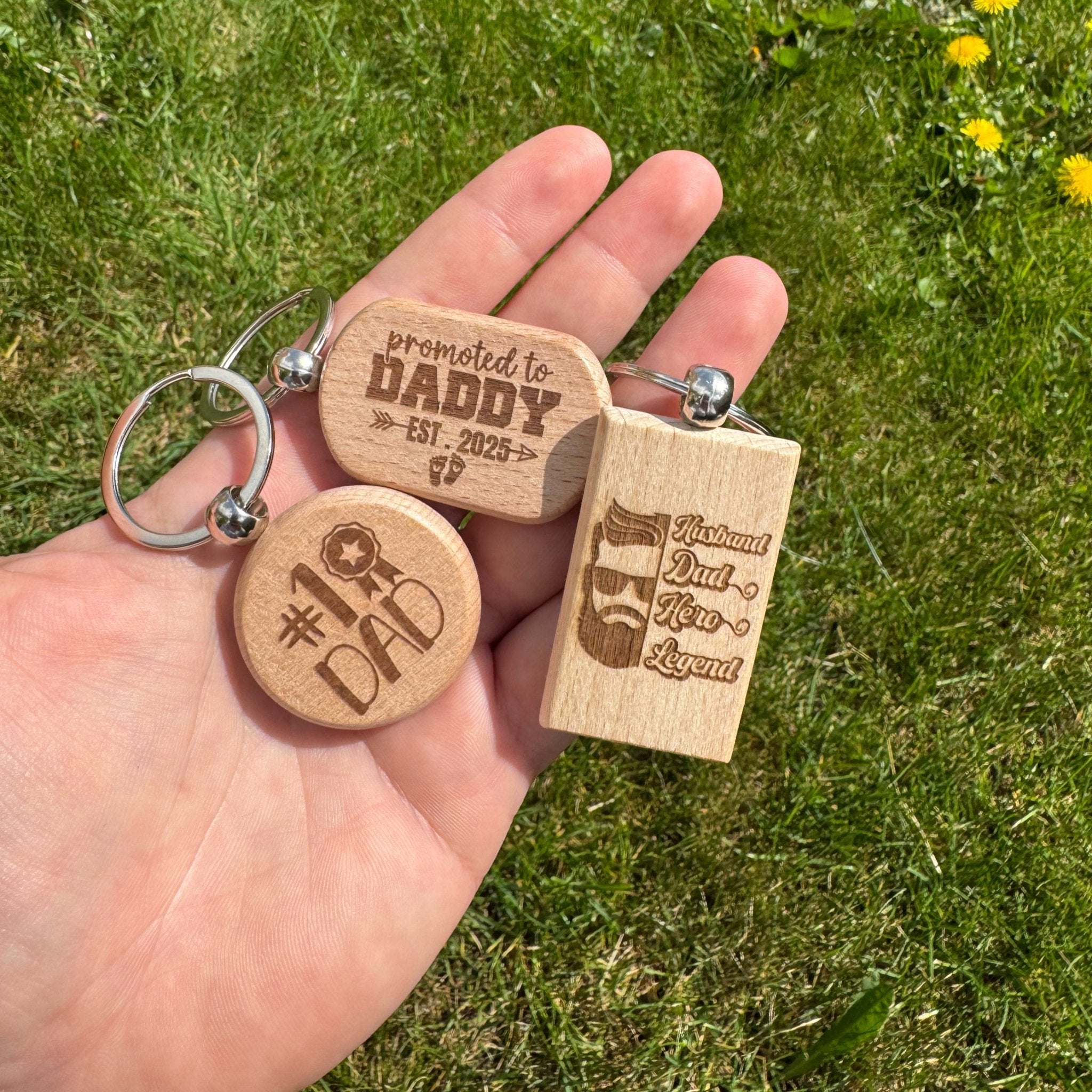 Three laser-engraved wooden keyrings with custom text, shown outdoors – personalised wooden keyrings – Etch 'N' Shine