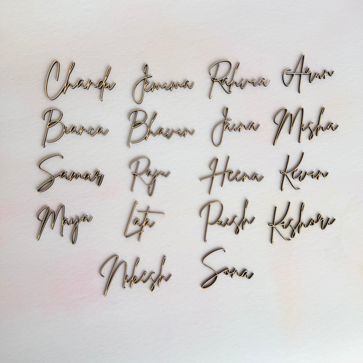 Custom wooden name place settings displayed for wedding table seating, personalised script names cut from natural plywood