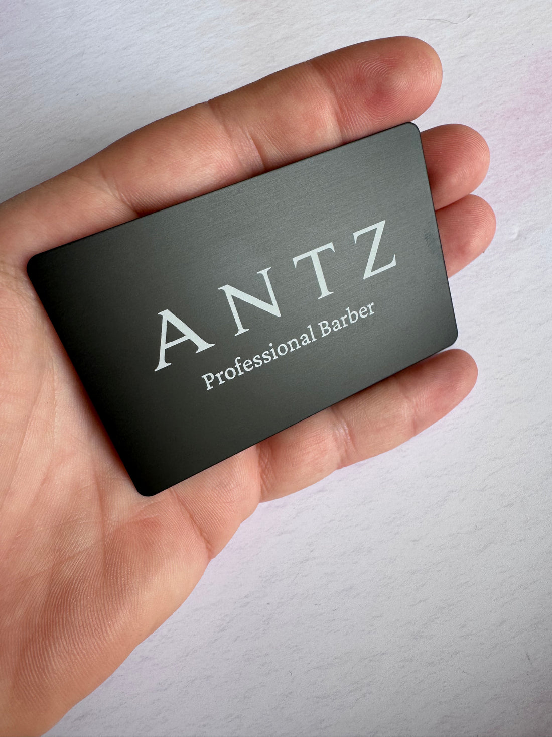 Black anodised aluminium business card held in hand with engraved barber branding