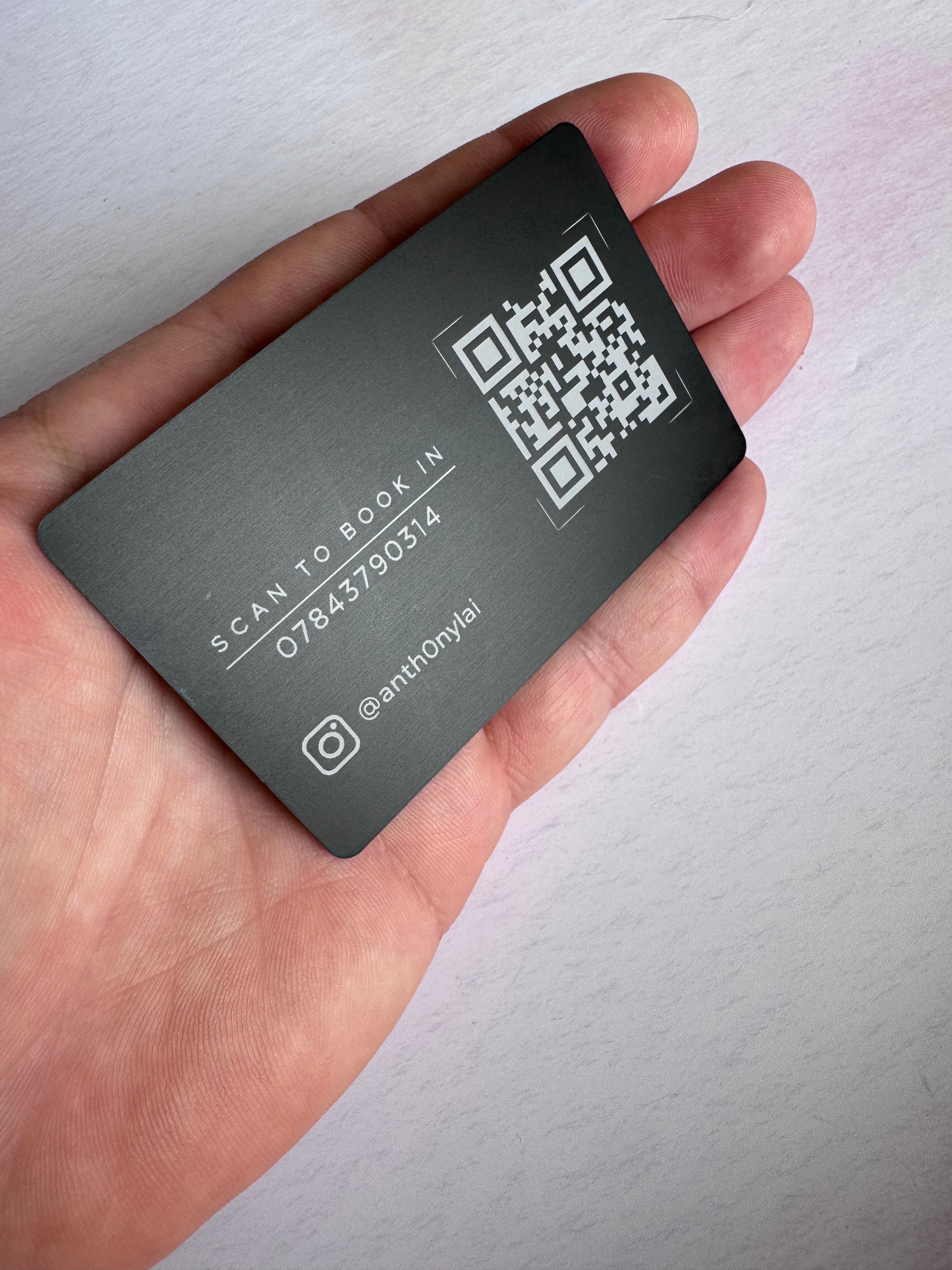 Reverse of a black anodised aluminium business card held in hand with engraved QR code and business contact details