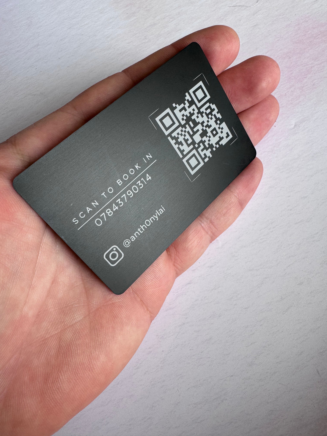 Reverse of a black anodised aluminium business card held in hand with engraved QR code and business contact details