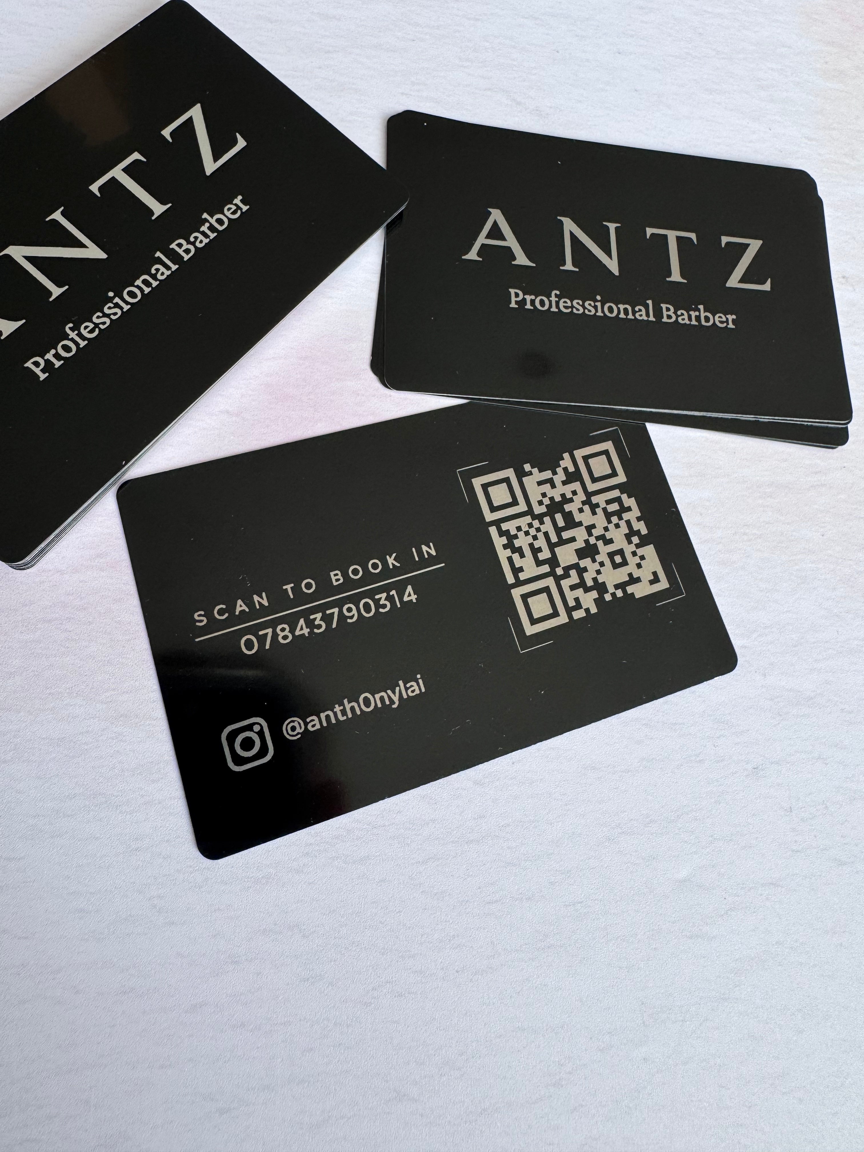 Front and reverse sides of personalised black anodised aluminium business cards with barber logo and QR code