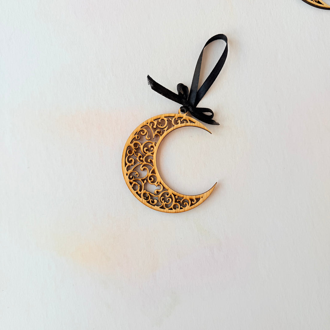 Decorative gold crescent moon ornament with black ribbon on a light gray background