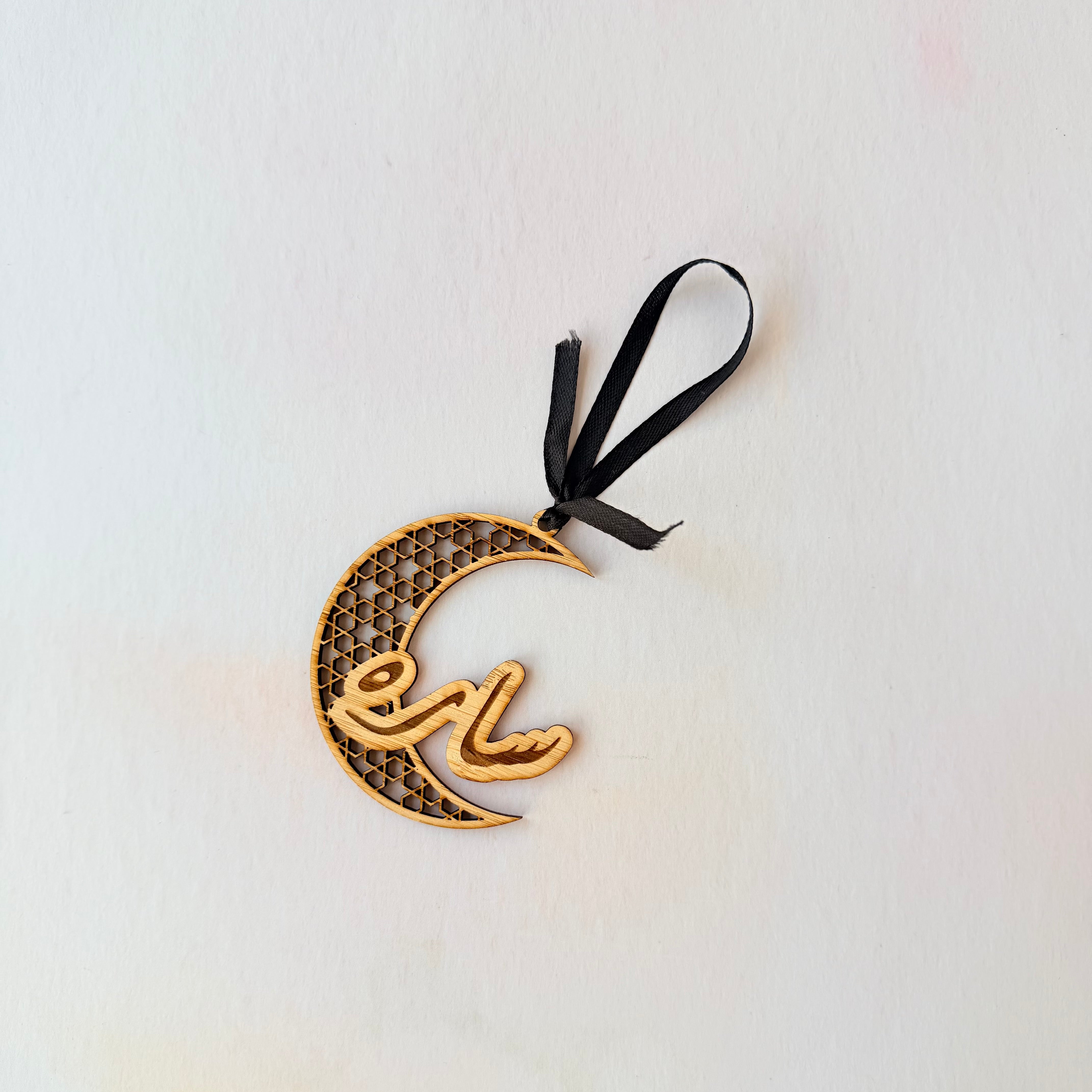 Decorative crescent moon ornament with Arabic text on a white background