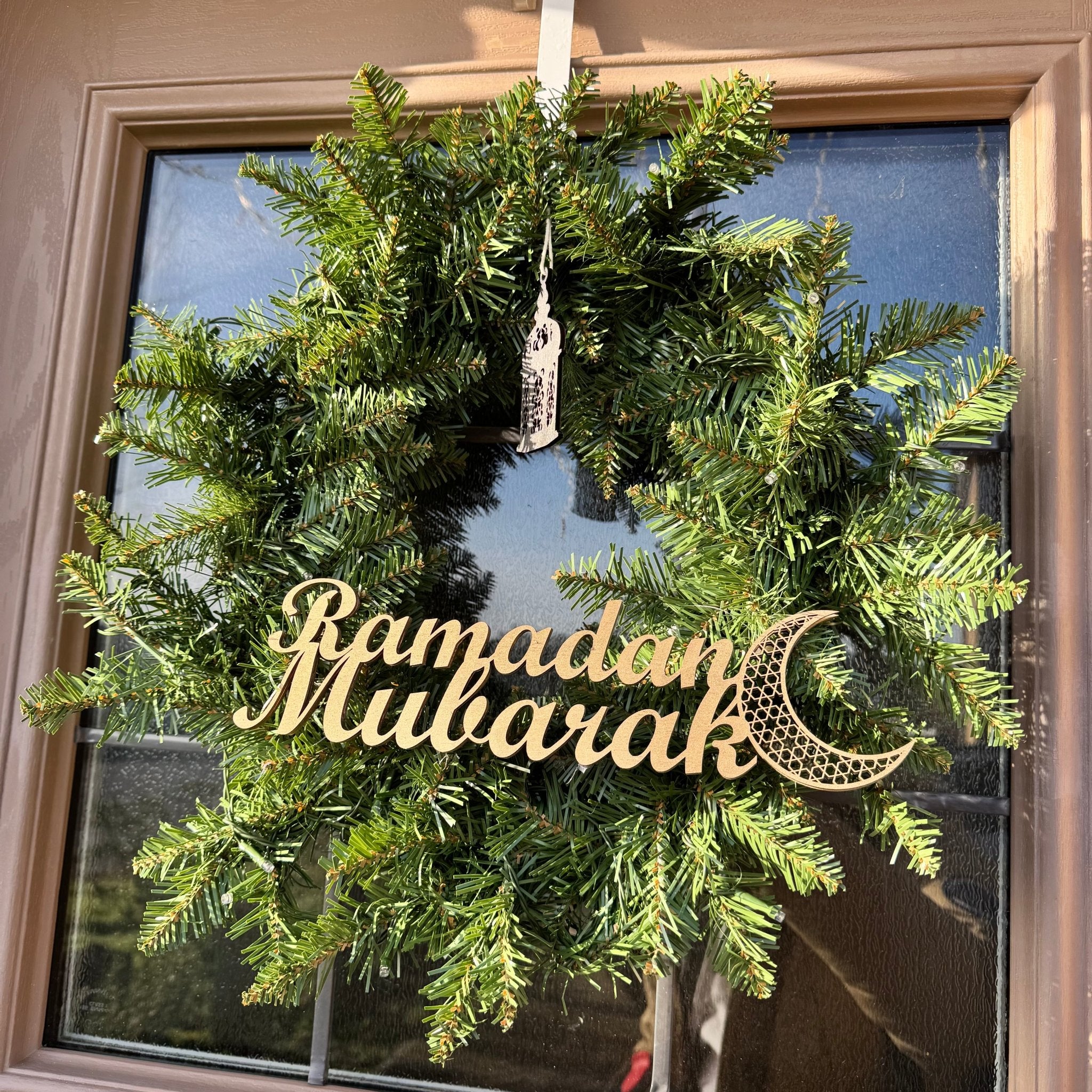 Laser-cut wooden Ramadan Mubarak sign with crescent moon detail on a green wreath hung on a front door – Etch 'N' Shine