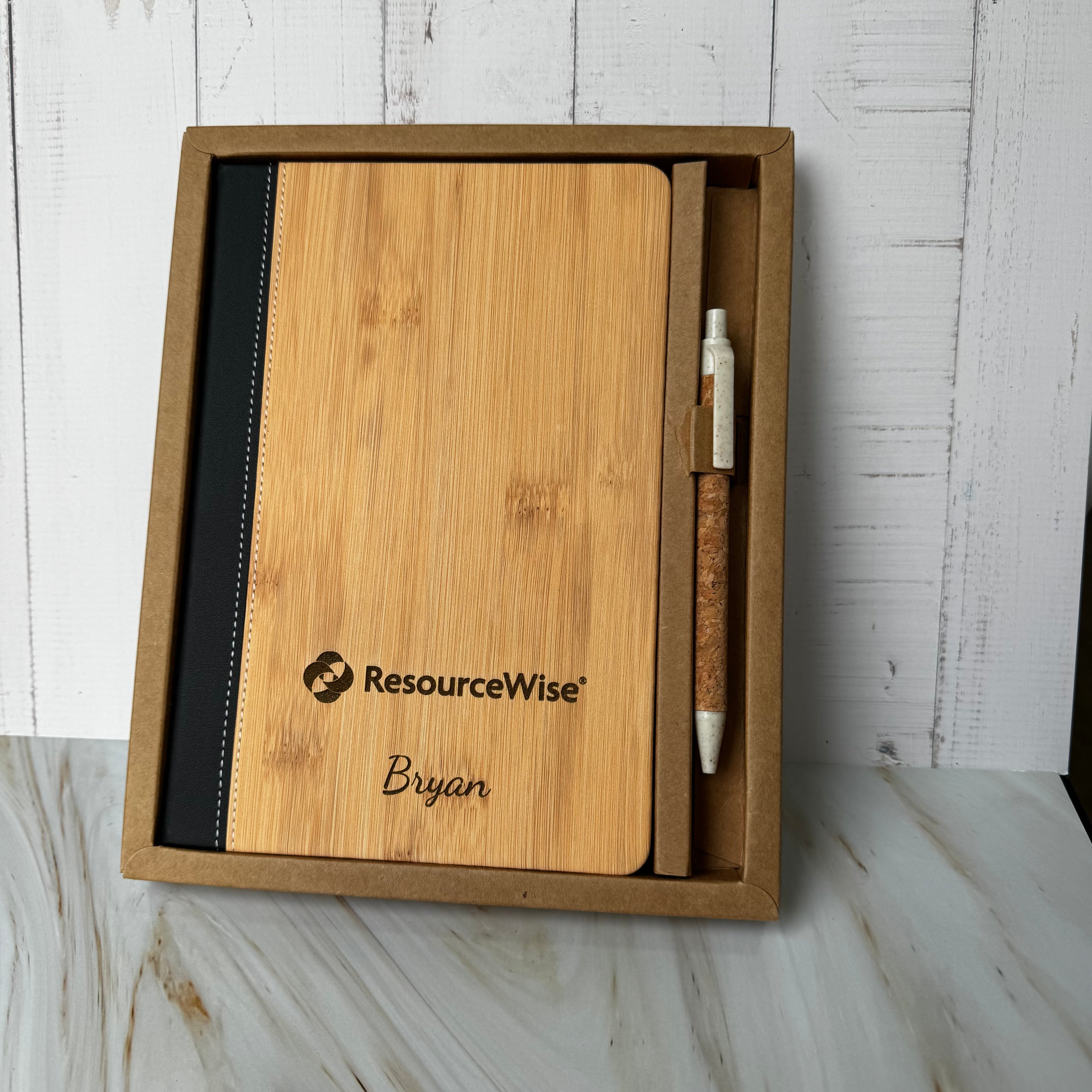 Wooden notebook and pen set with 'ResourceWise' branding in a box on a wooden surface.