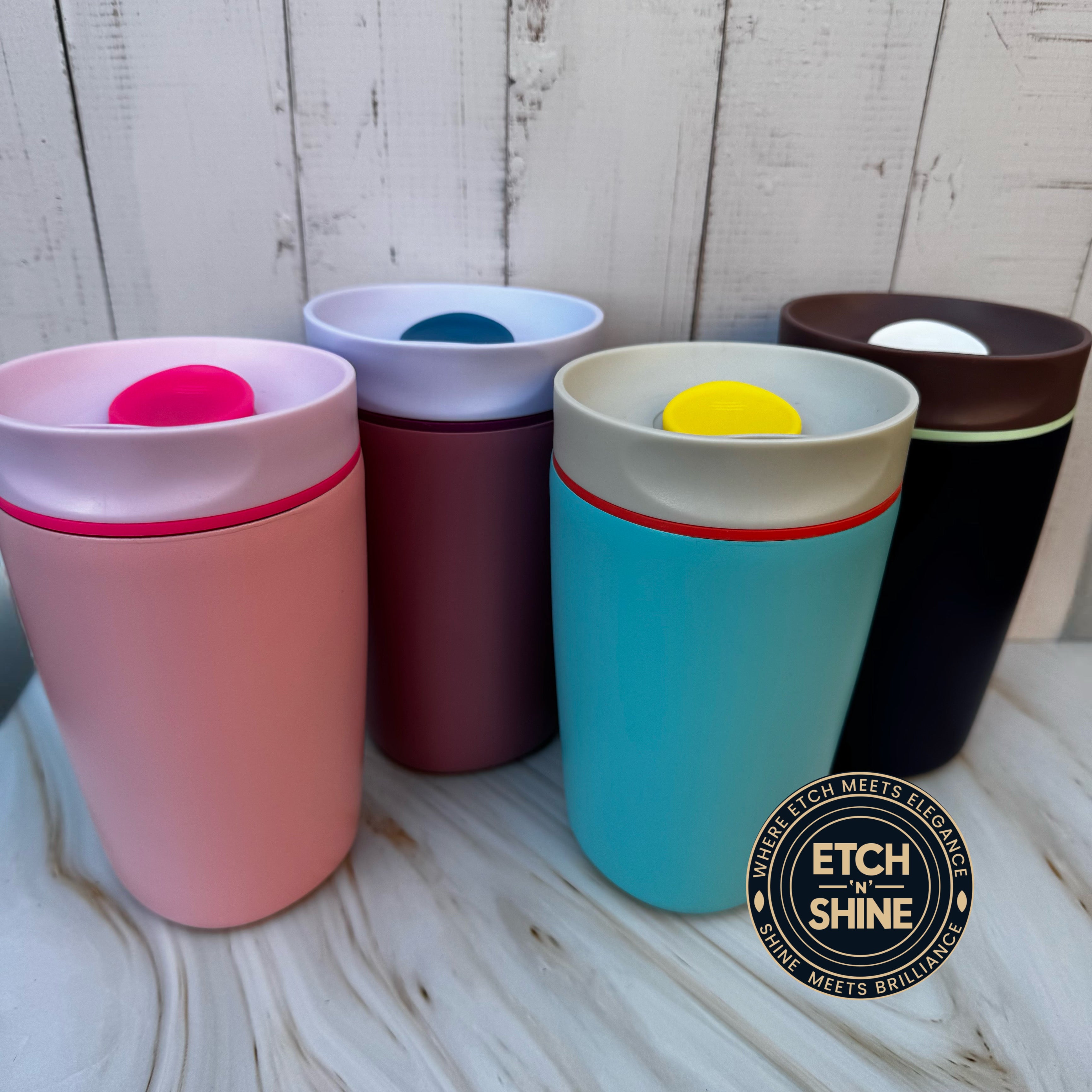 Set of colorful tumblers with Etch 'n Shine logo on a wooden surface