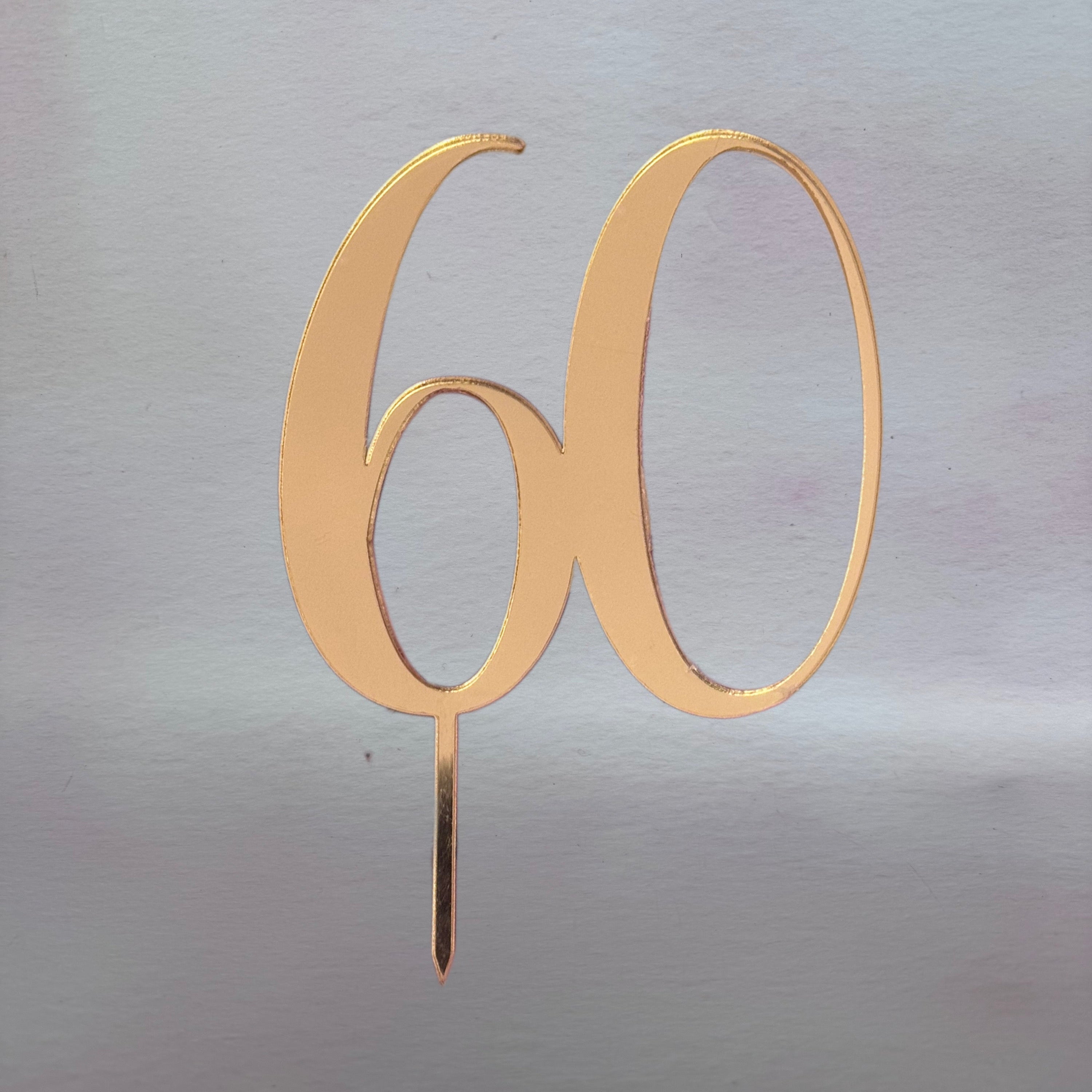Gold number '60' cake topper on a reflective silver background