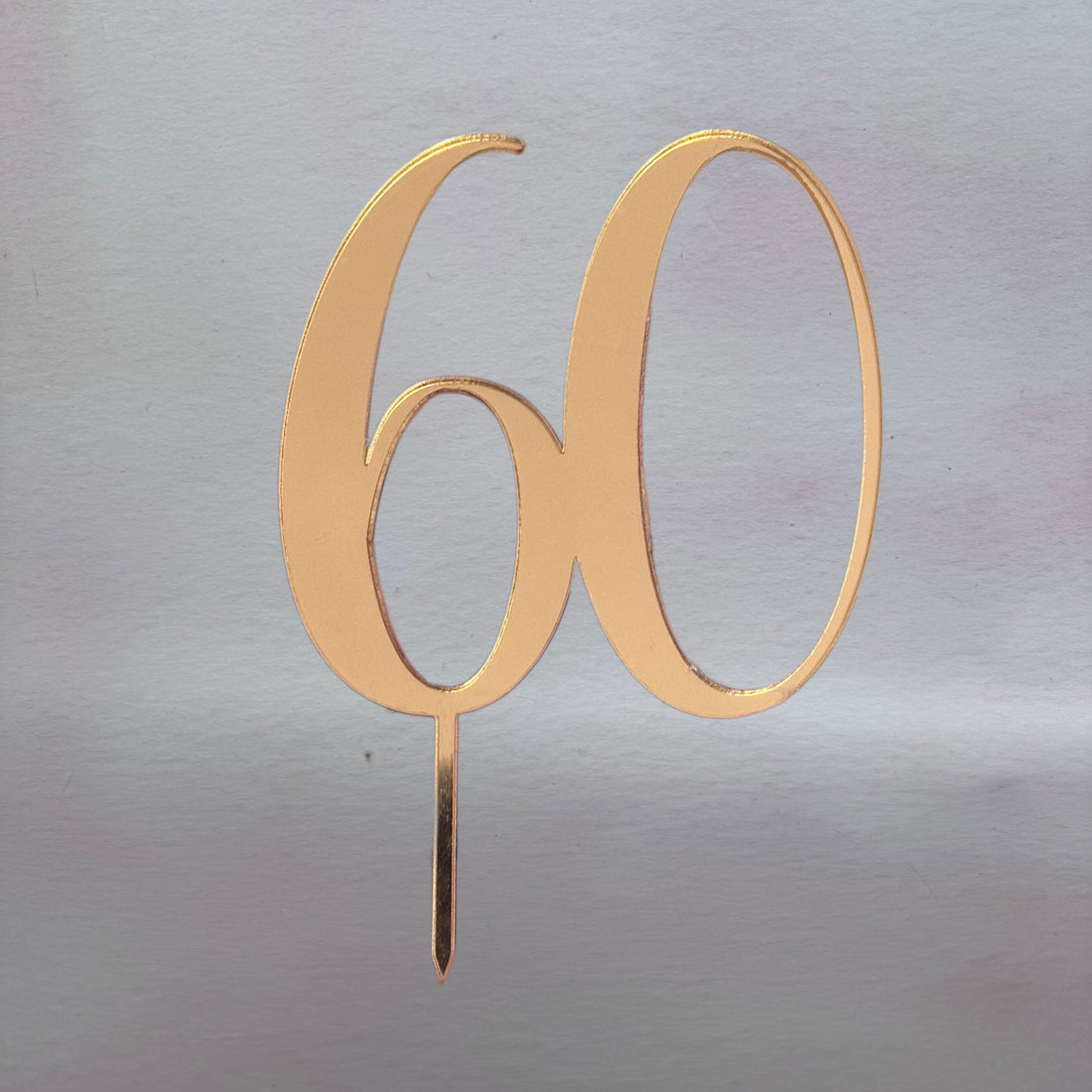 Gold number '60' cake topper on a reflective silver background