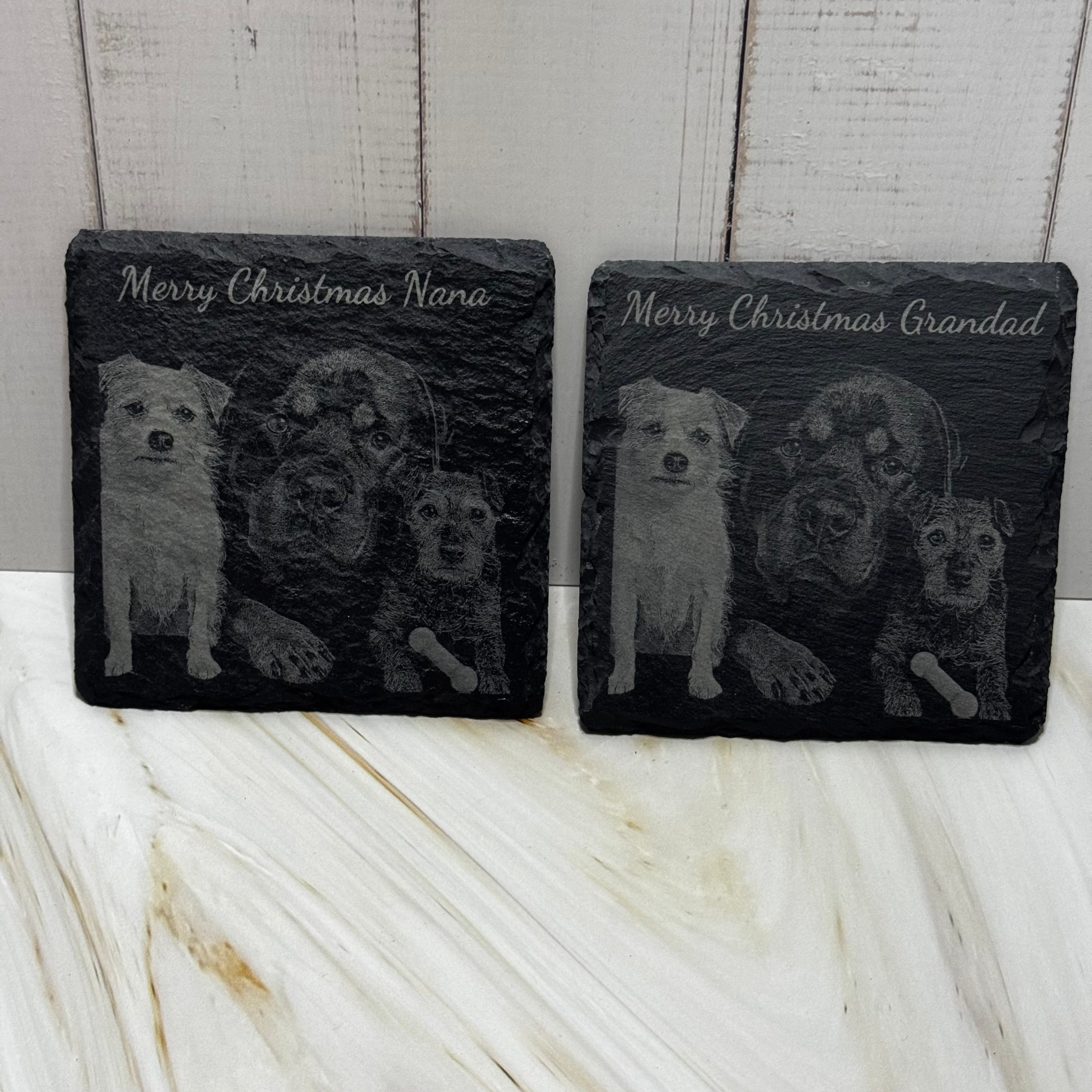 Two slate coasters with engraved images of dogs and text on a wooden surface.