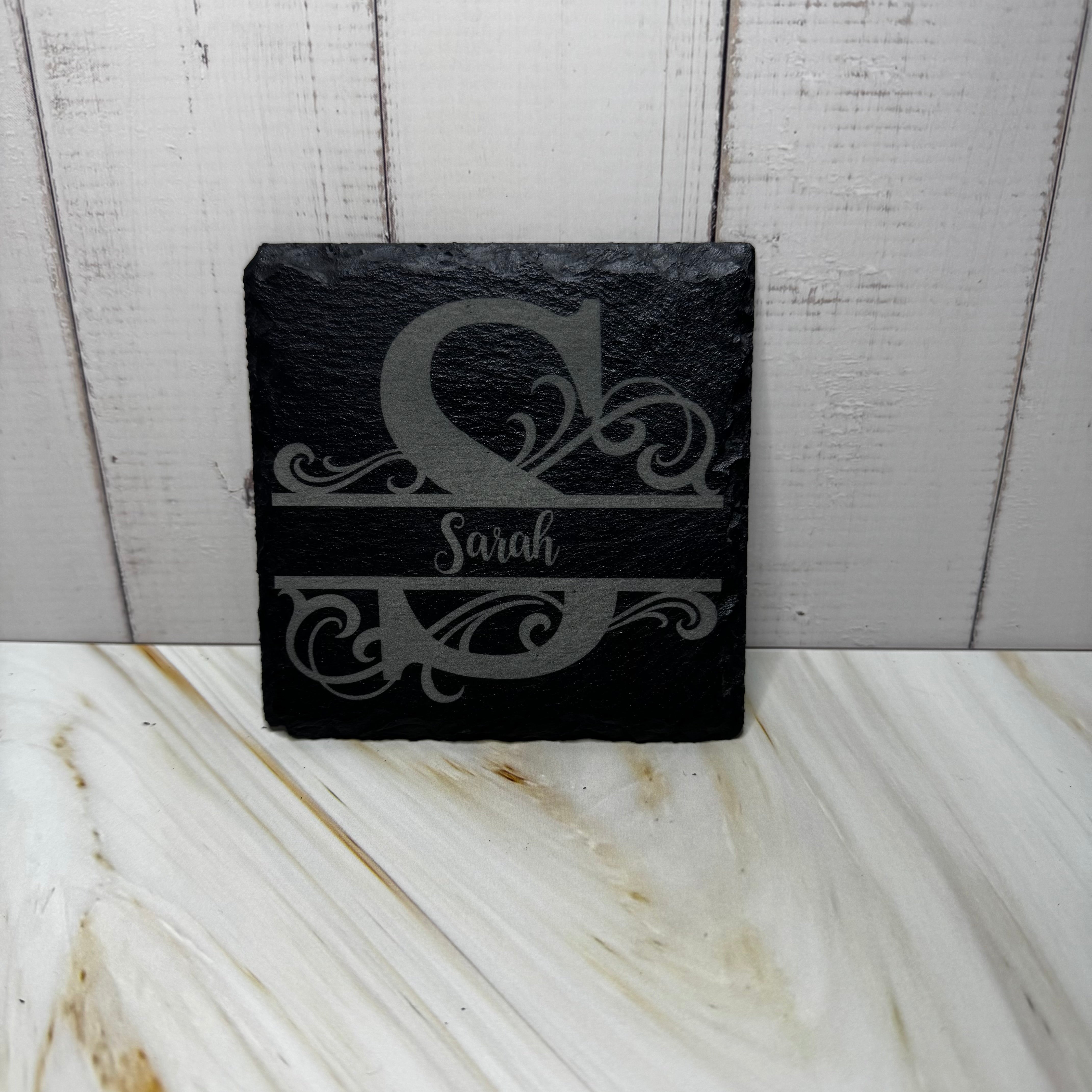 Black slate coaster with engraved monogram and name on a marble surface
