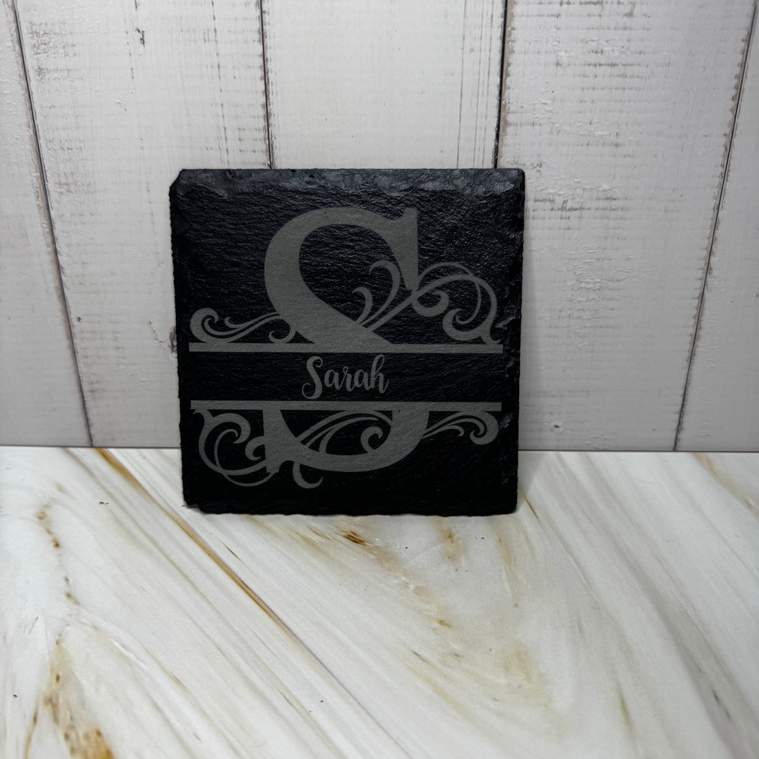 Black slate coaster with engraved monogram and name on a marble surface