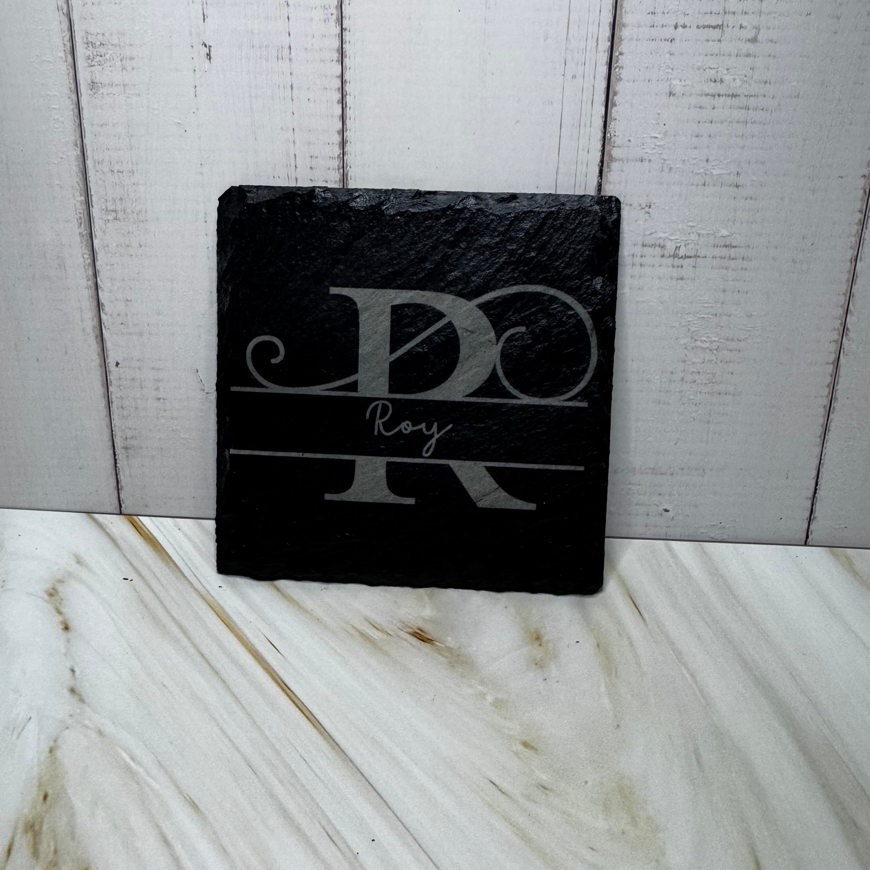 Black slate coaster with engraved initials on a marble surface