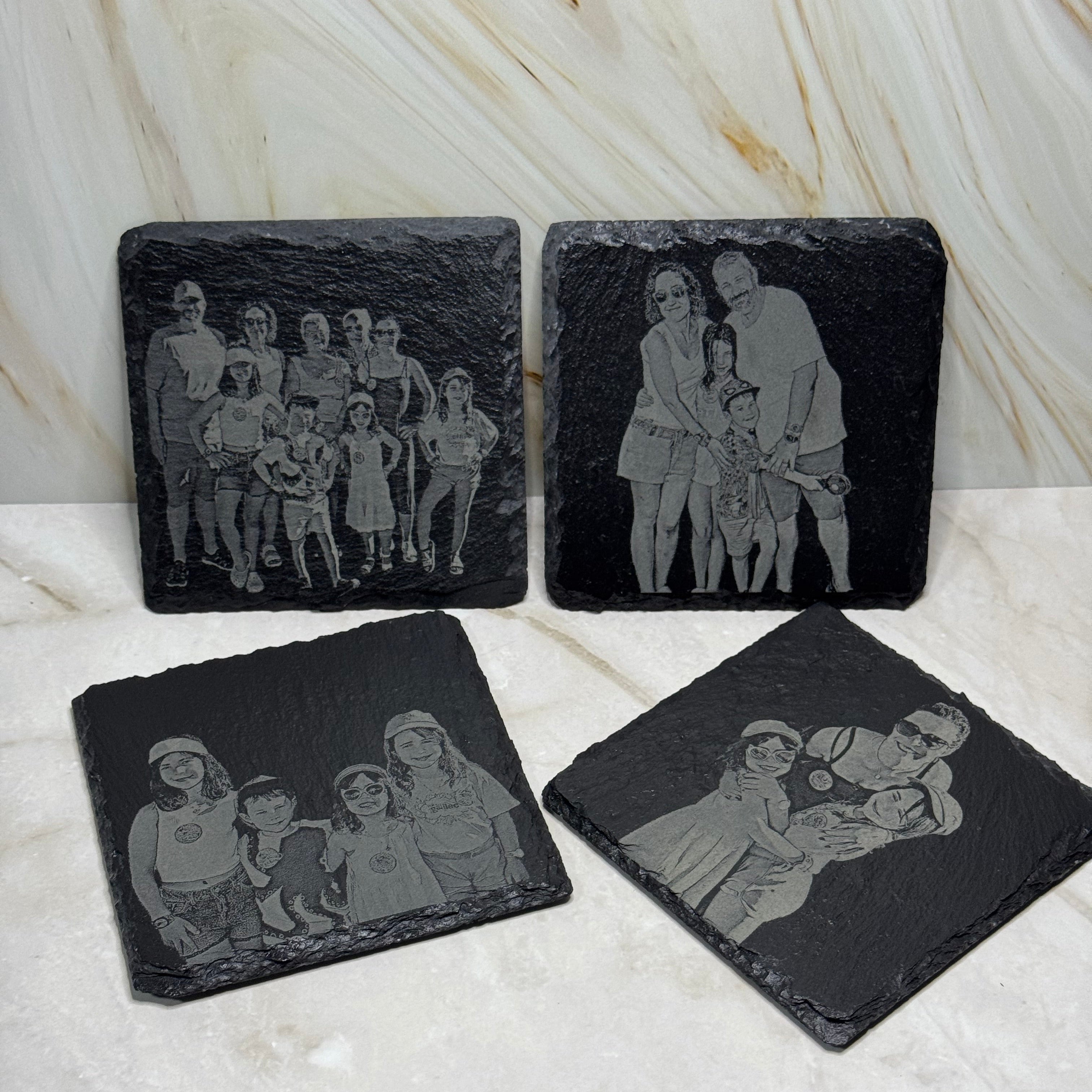 Four black stone coasters with engraved images on a marble surface