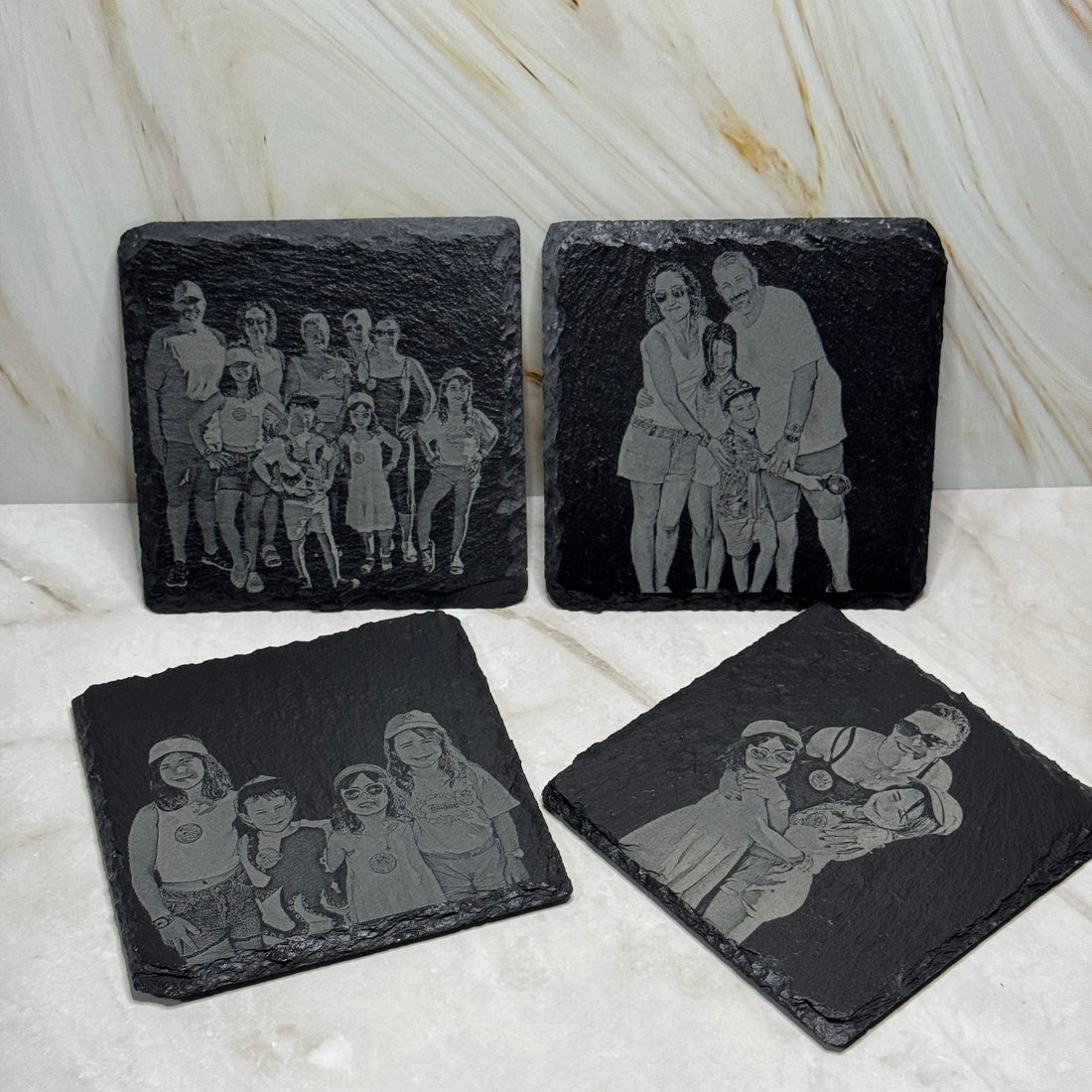 Four black stone coasters with engraved images on a marble surface