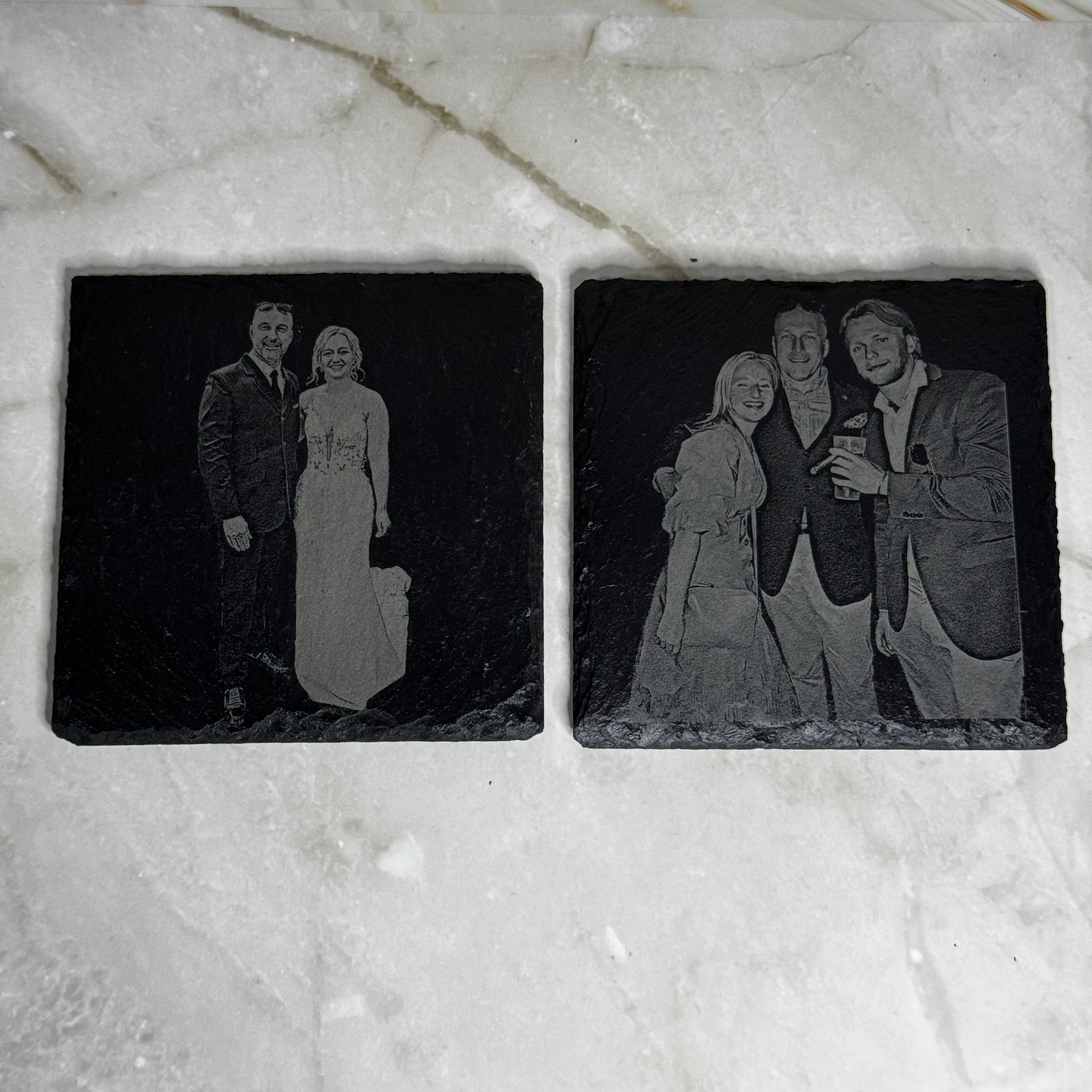 Two engraved black stone coasters with images of people on a marble surface.