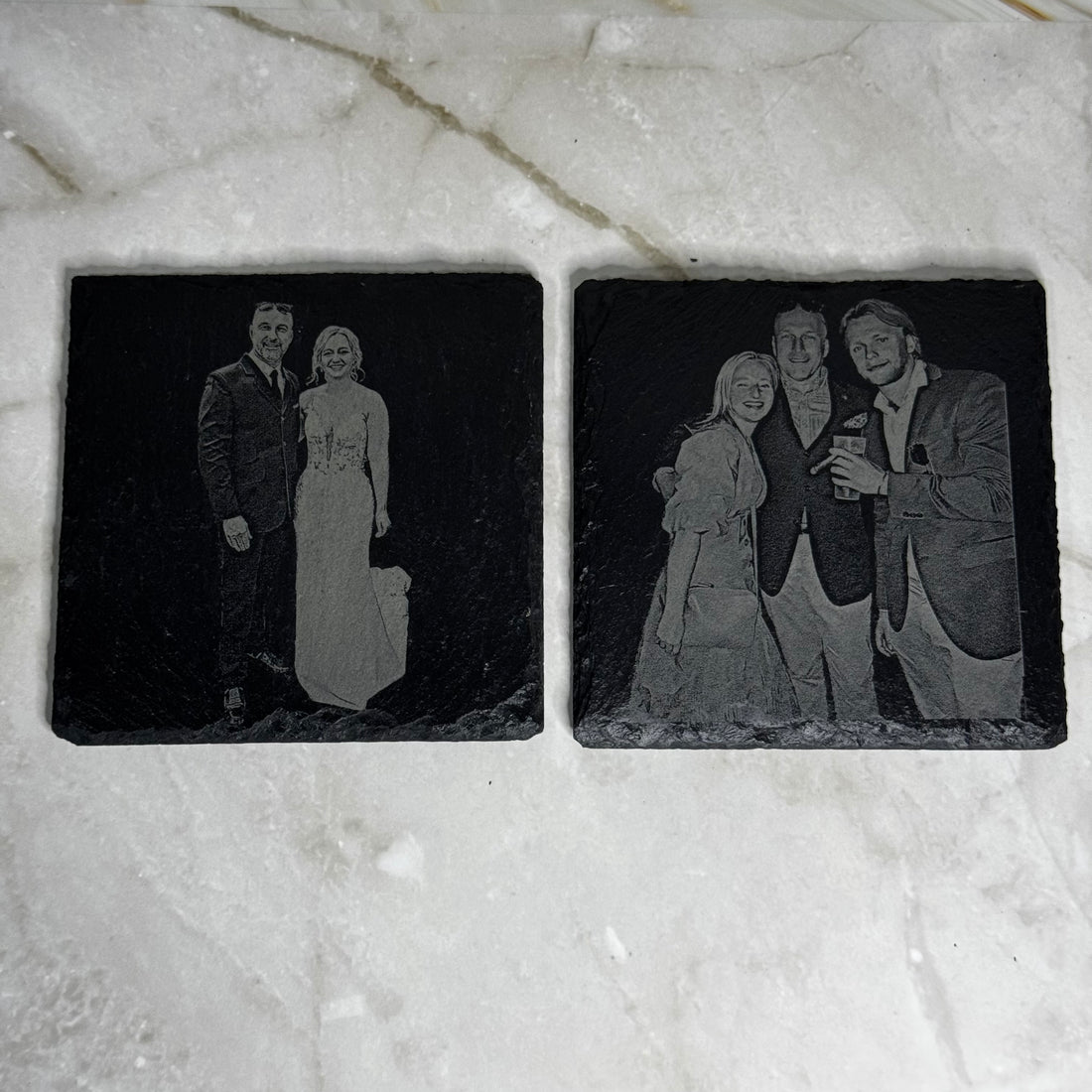 Two engraved black stone coasters with images of people on a marble surface.