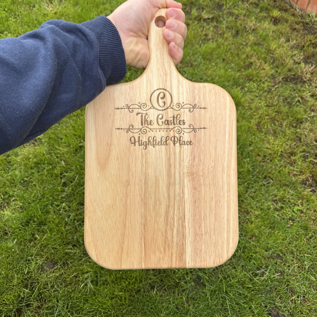 Wooden paddle board with engraved text held by a person on grass