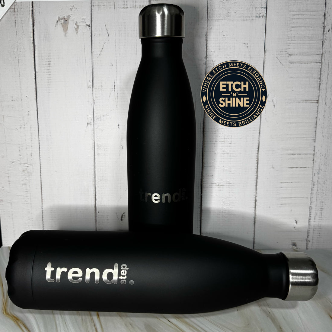 Black water bottle with 'trend' branding on a wooden surface, featuring Etch 'n Shine logo.