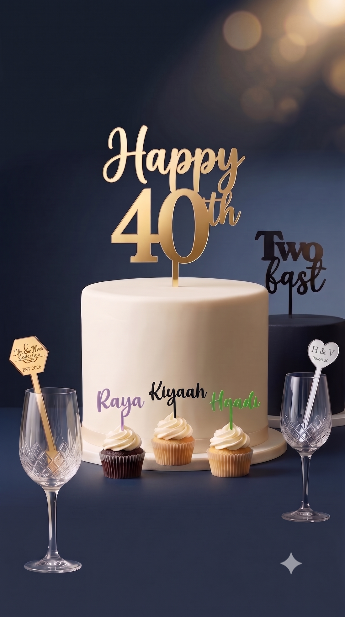 A white frosted birthday cake with gold 'Happy 40th' lettering topper, surrounded by three cupcakes, two crystal wine glasses, and small custom picks on a dark navy background.