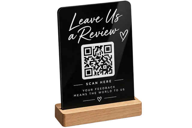 Black acrylic "Leave Us a Review" QR code sign on a wooden counter stand